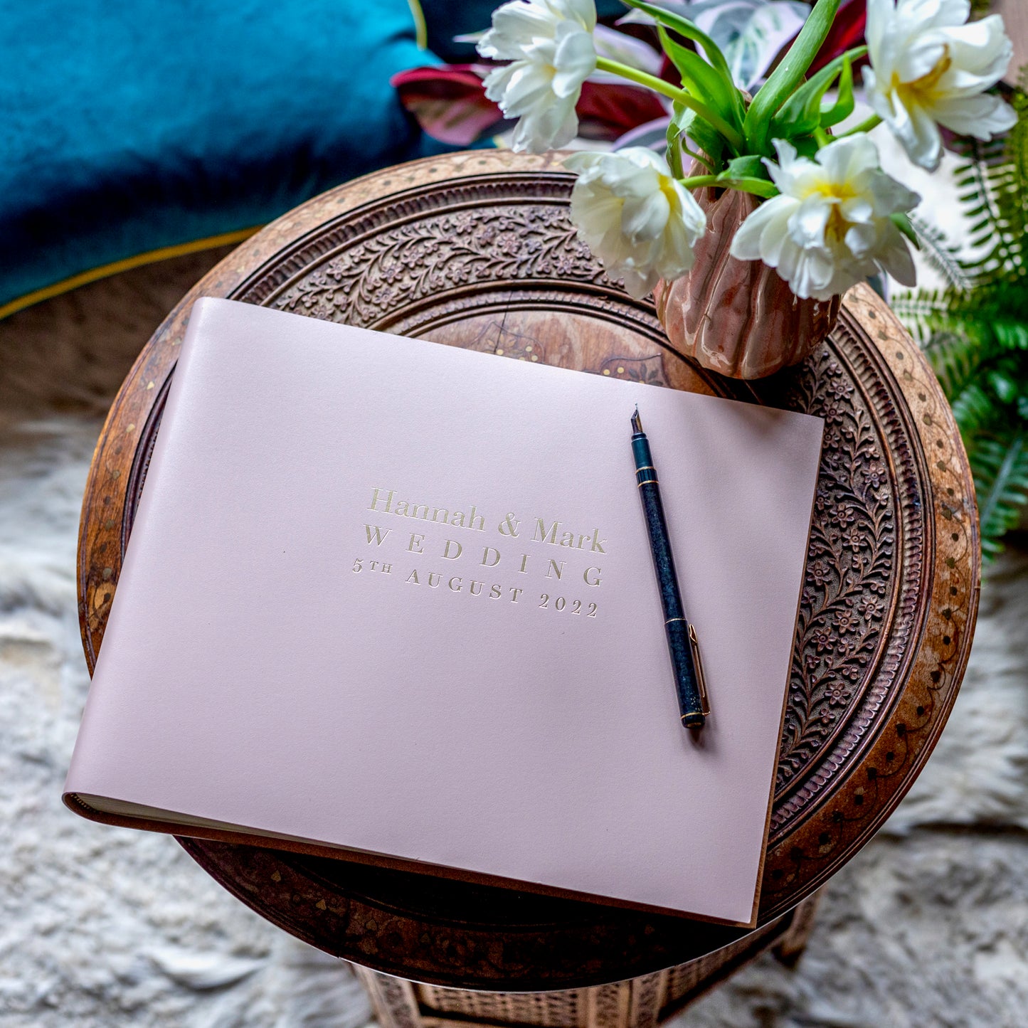 Baby pink coloured wedding guest book resting on a small table