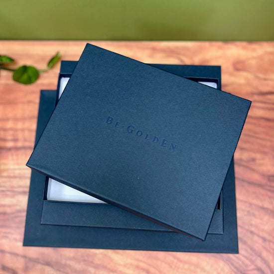 a set of navy blue presentation boxes are on a wooden table and you can see that they have been embossed with the company name BeGolden
