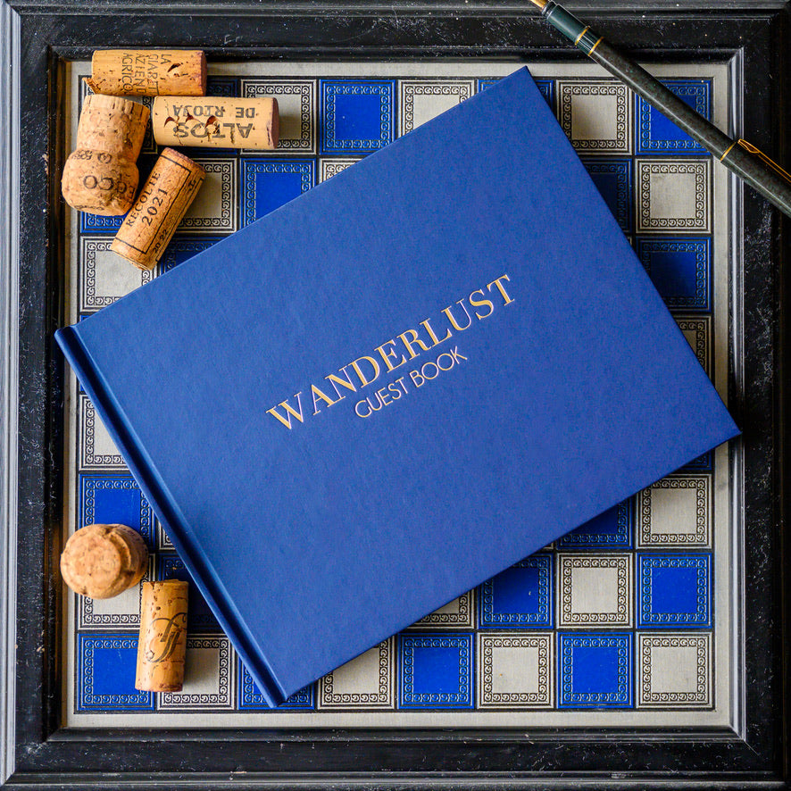 China Blue hardback guest book embossed with the words 'Wanderlust', with wine corks on a decorative background