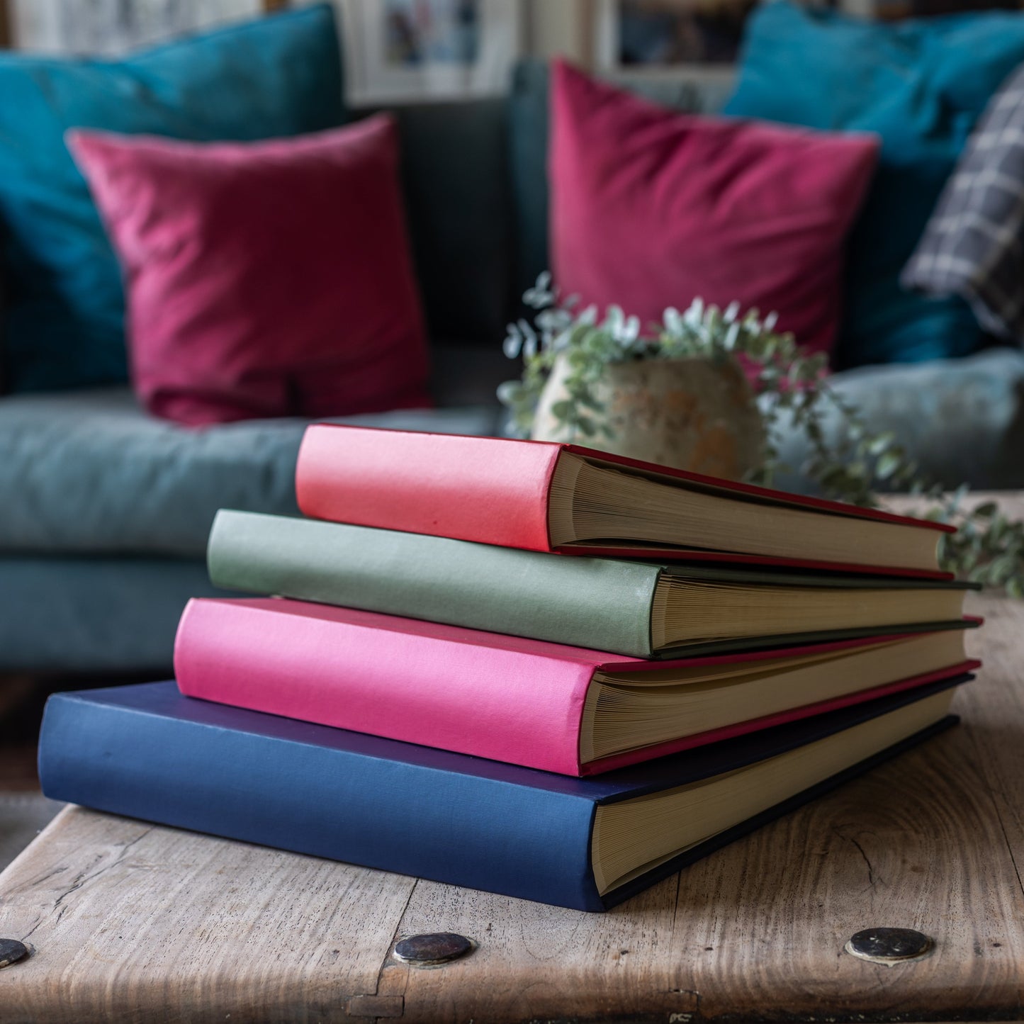 Stack of colorful photo albums on a wooden table with a blurred background of a living room.