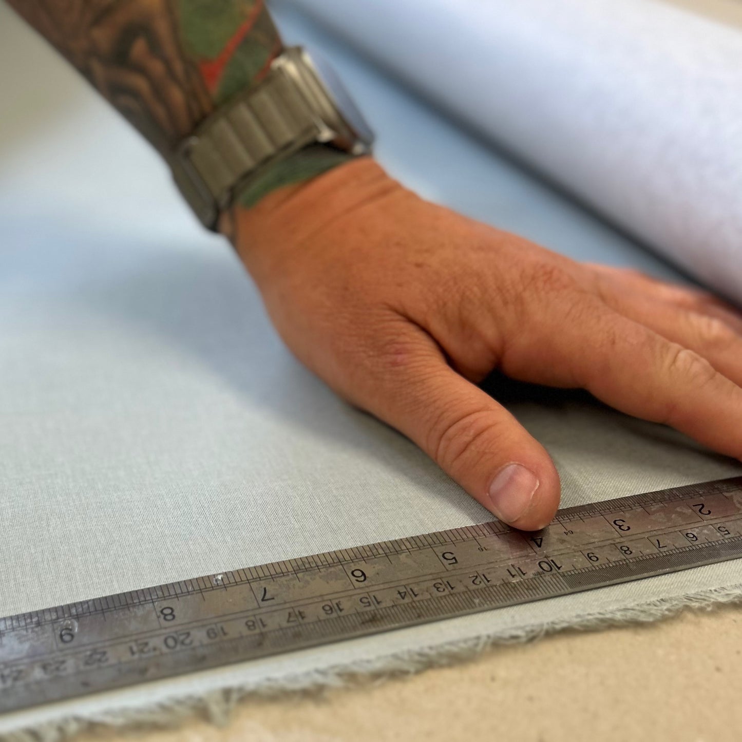 A man is measuring the light blue book cloth with a metal ruler.