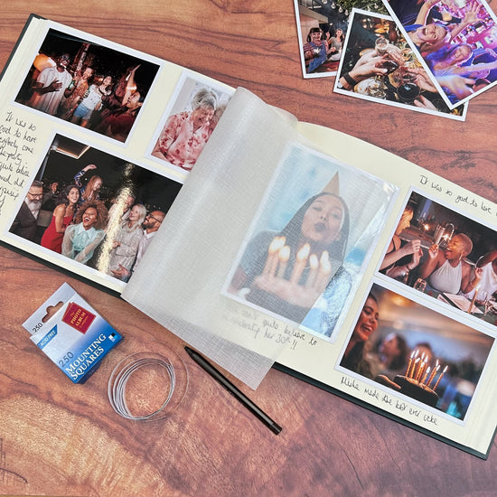 a large wedding album lies open on a coffee table. It is full of wedding photos and lots of messages. There are photo by the side and mounting squares