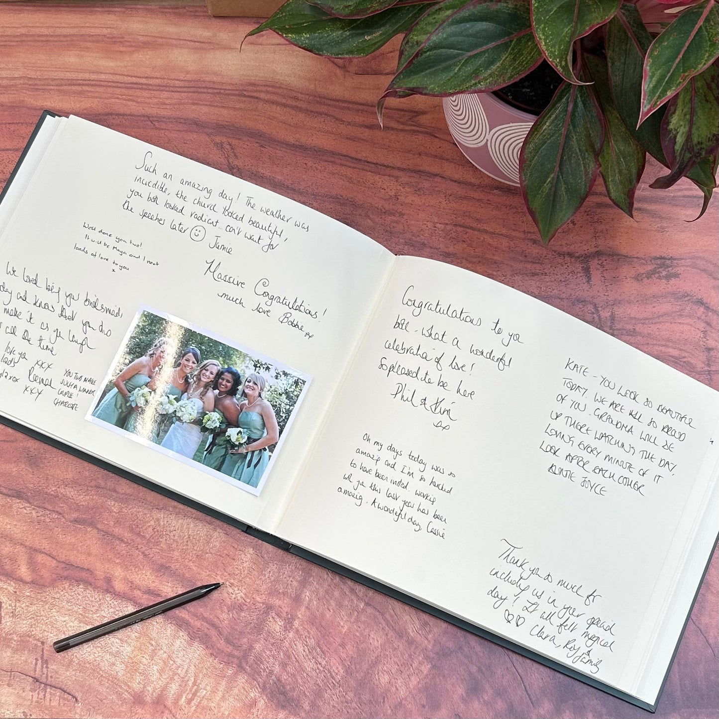 an open wedding guest book is on a wooden table. the wedding guest book has been signed by lots of guests with messages. there is also a wedding photo in the guest book