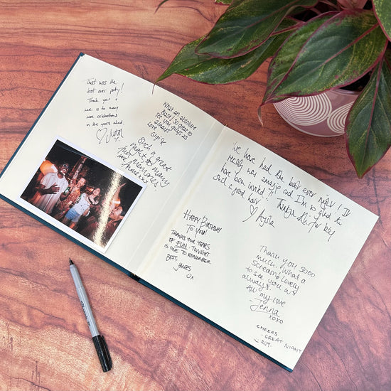 on a wooden coffee table is a wedding guest book which has been signed by all the guests. There is also a photo in the wedding guest book of a party