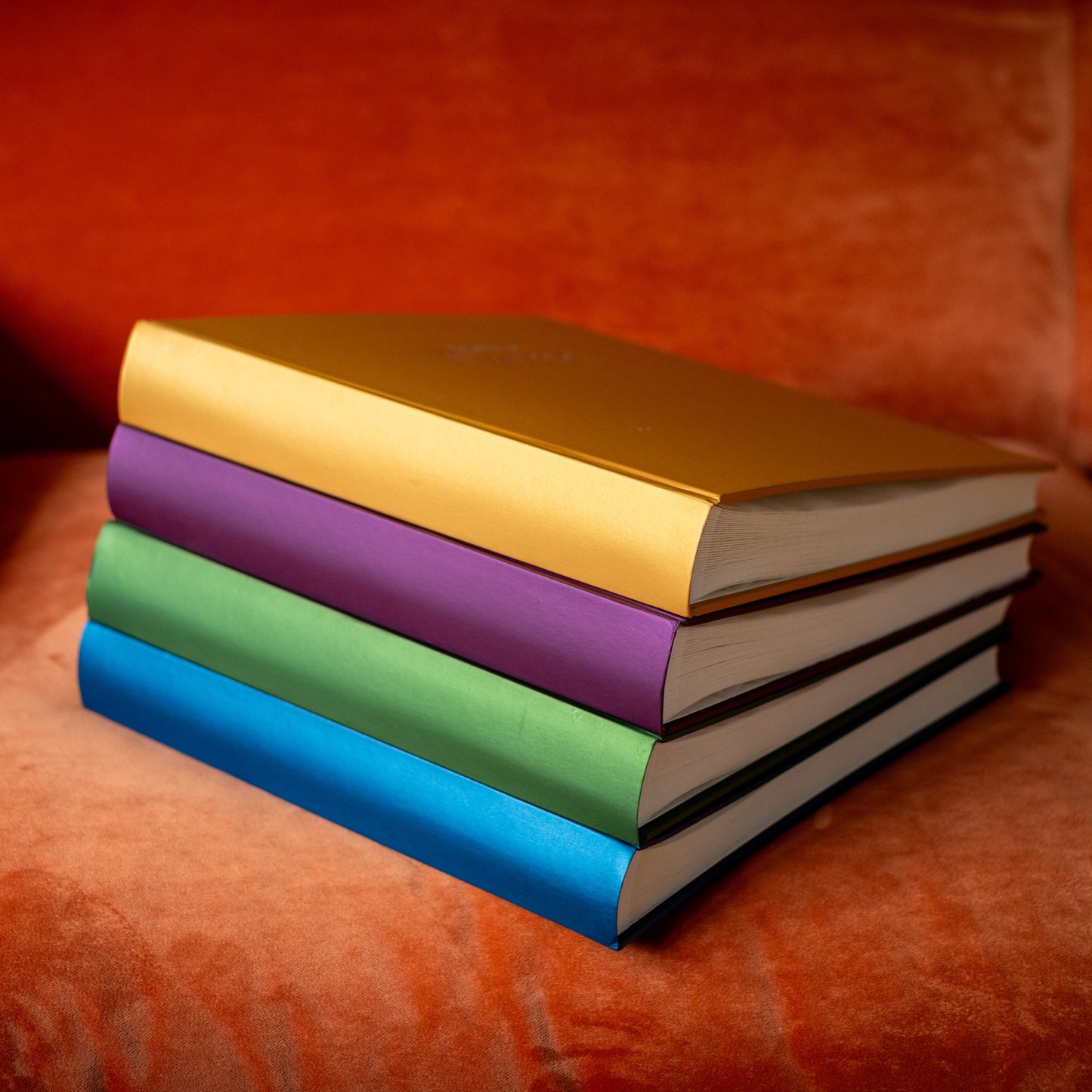 There are four jewel albums stacked on top of one another. They are placed on an orange velvet sofa.