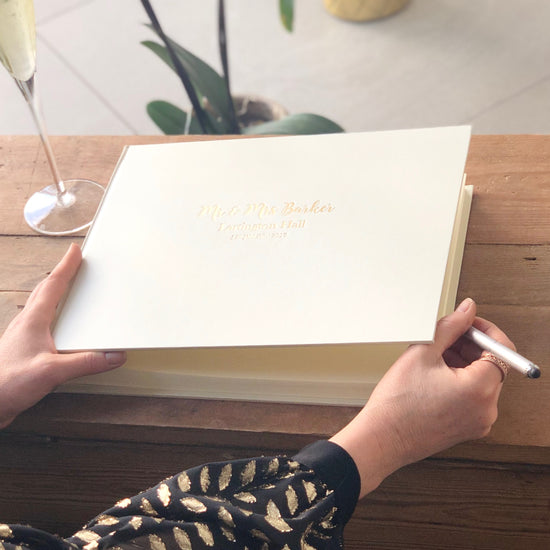 someone holds a pen in their hand ready to write a message in the wedding guest book