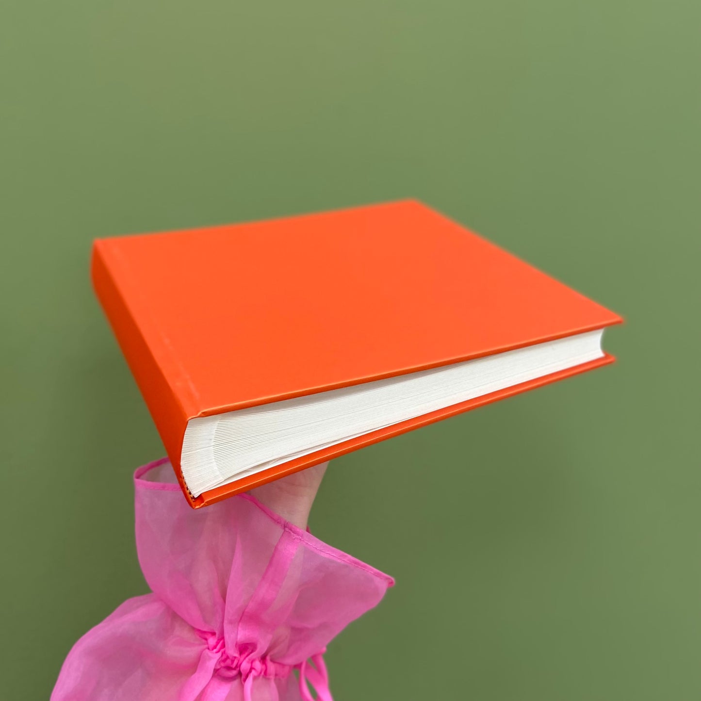 an orange wedding guest book is being held up so you can see the traditional binding. the background is green