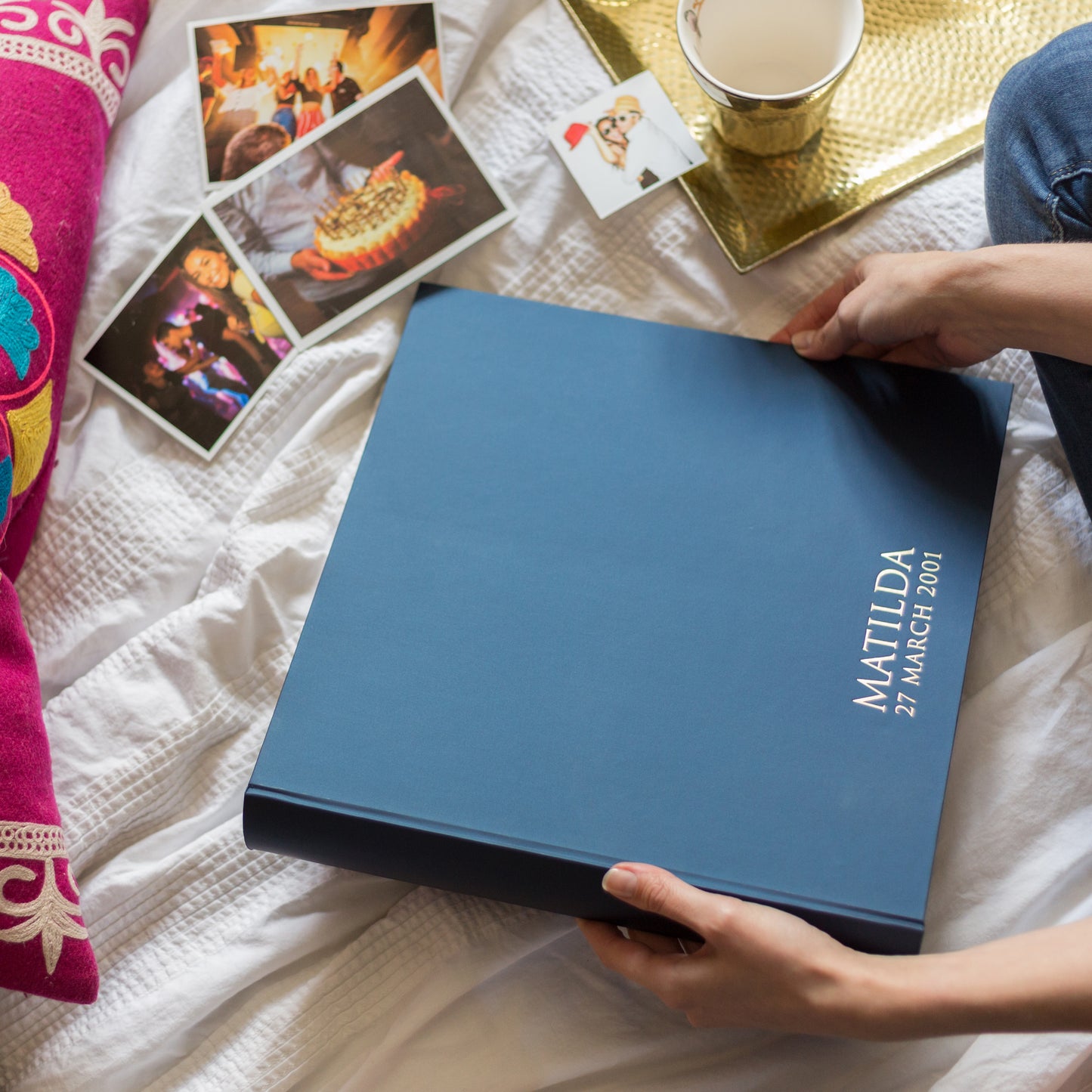 a woman is sitting on her bed and is looking through her large blue photo album. The photo album has been personalised with a name at the bottom 