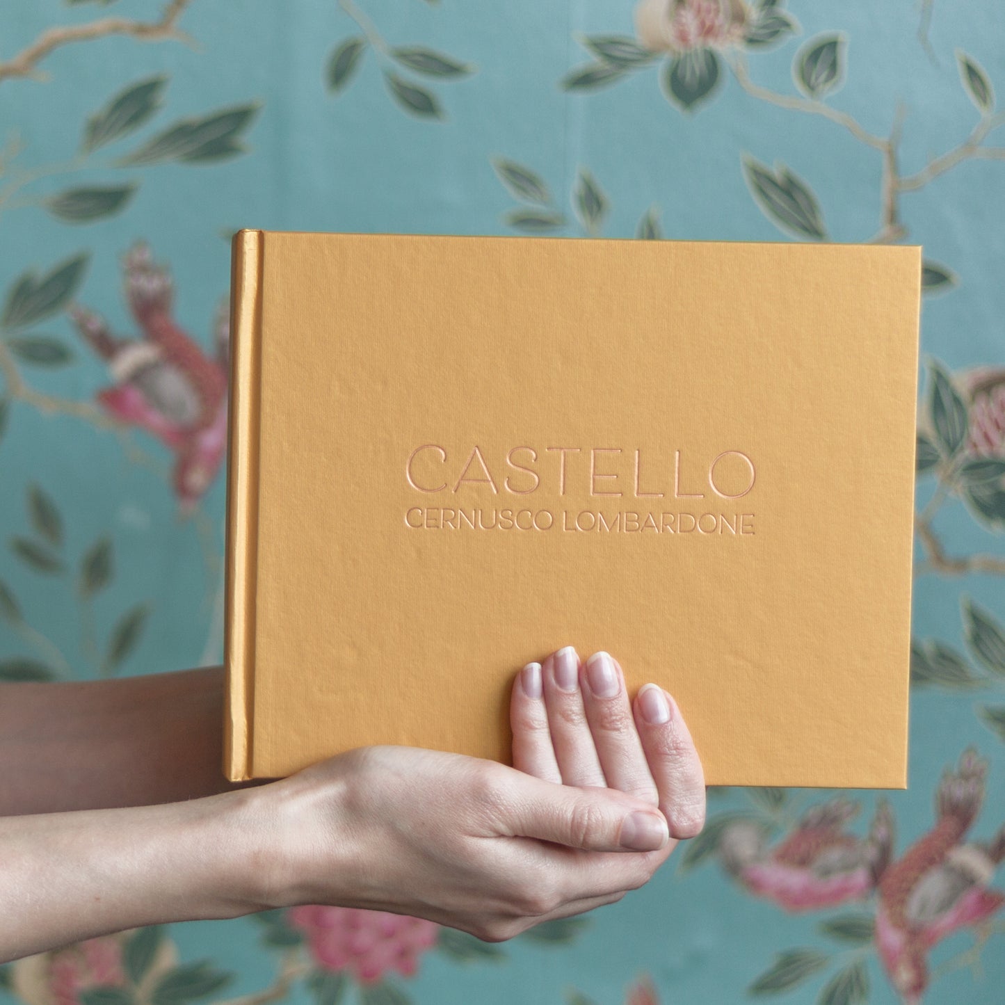 against a flowery background a woman holds a yellow guest book that has been printed with the name of a house