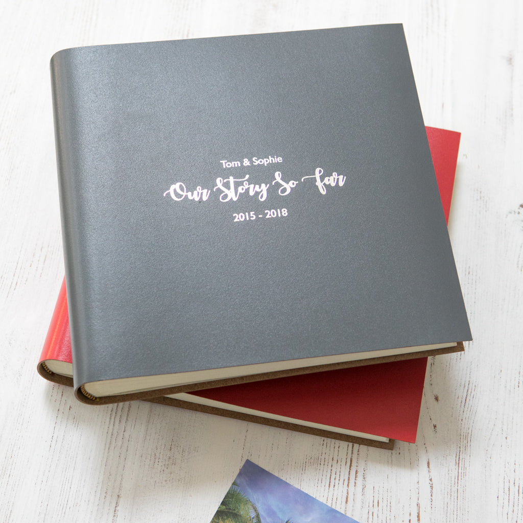 a grey square family album sits on top of a red album. It has been printed with silver writing 