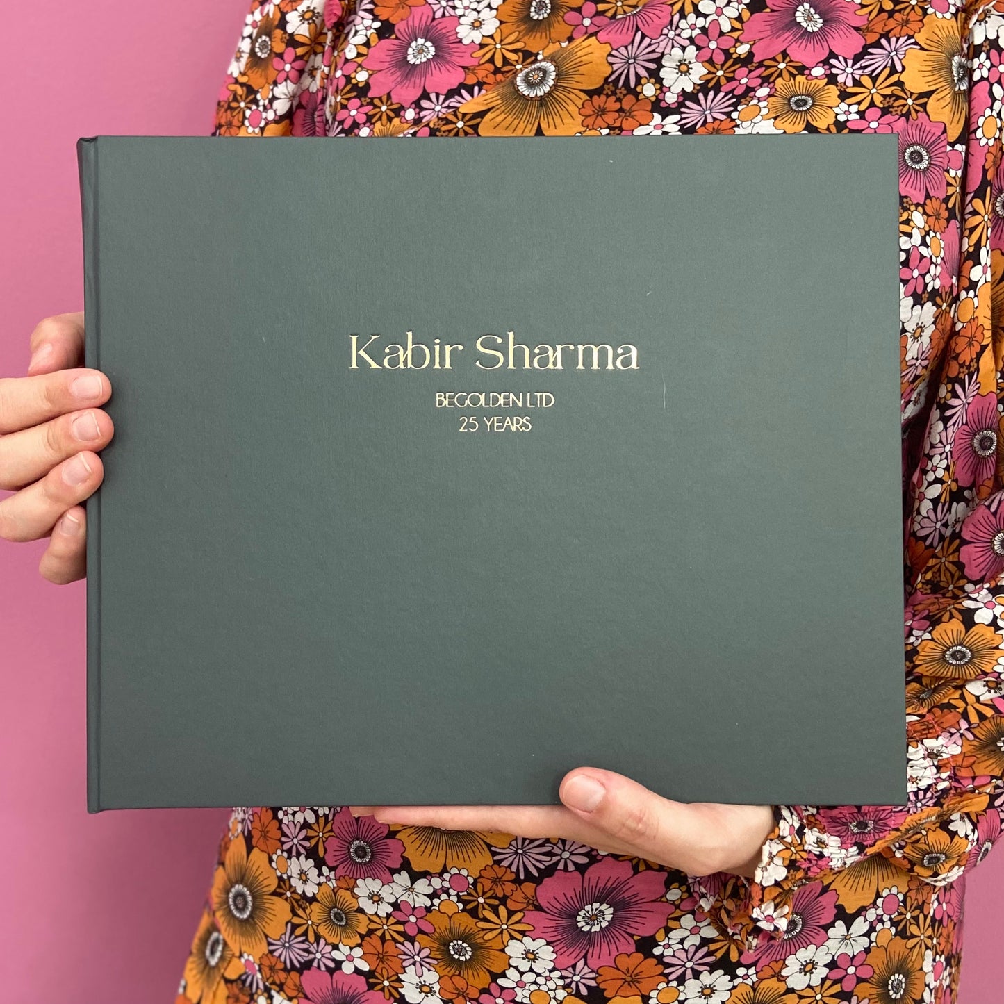 A woman is holding a large leavers book. It has a name and a company name printed on the front with gold hot foil.