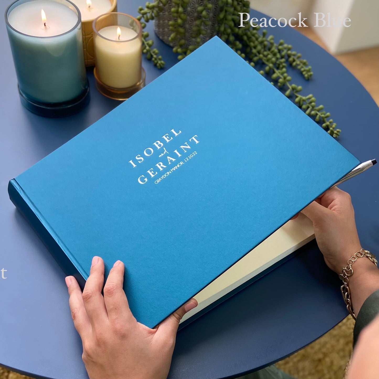 A woman is about to write a message in a peacock blue album. You can see the front of the album - where there are two names and a location personalised in hot foil.