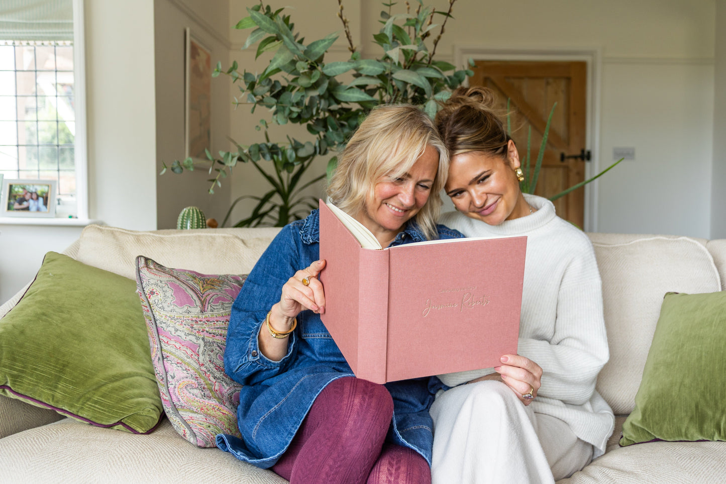 Two women sit on a sofa, reading from a personalised condolence book.