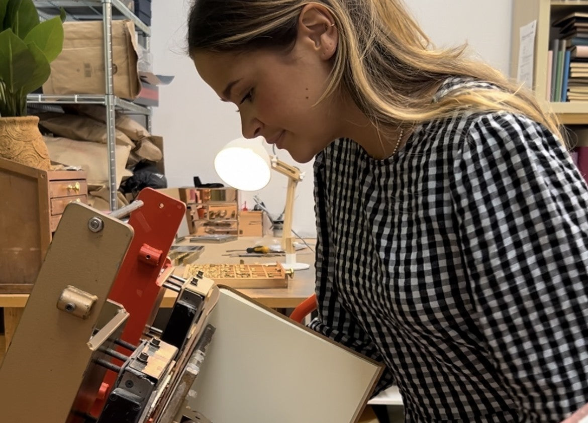 A young woman is hot foil printing a photo album by hand using a Marshall printing machine.