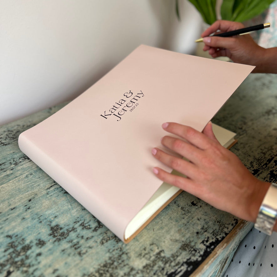 A wedding guest about to write in a baby pink coloured wedding guest book