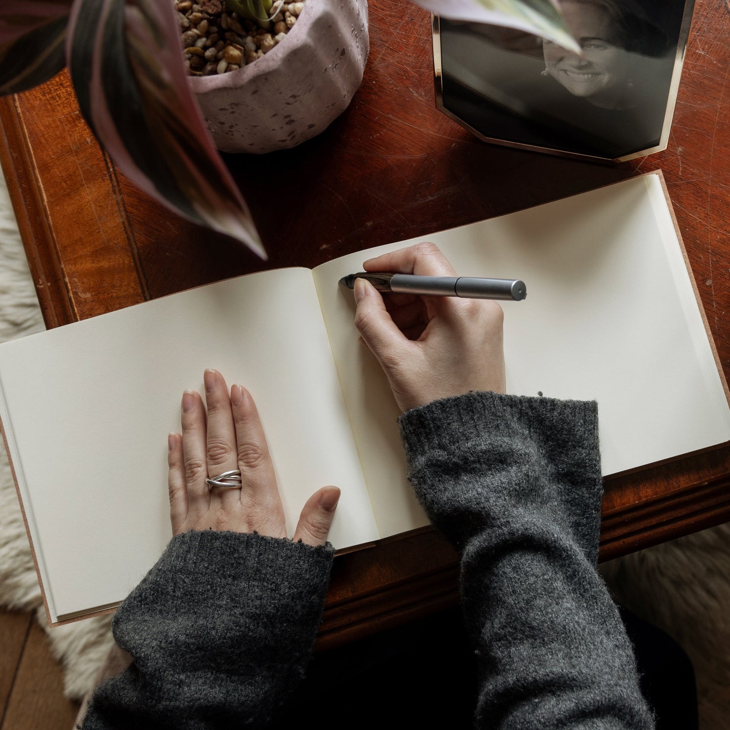 a large condolence book lies open on a wooden table and a woman in a grey jumper is poised with a pen and about to write a message in it