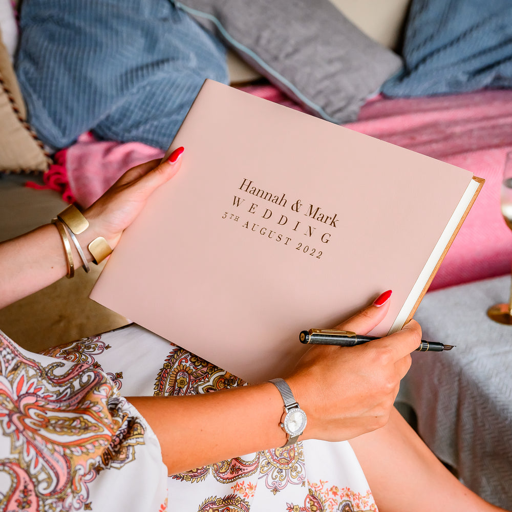 
                      
                        Wedding guest holding a guest book and pen in her hands admiring the front cover
                      
                    