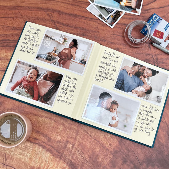 Load image into Gallery viewer, a baby memory scrapbook lies open on the table ad you can see it is full of photos and messages. There are lots of baby photos on the table and a packed of mounting squares
