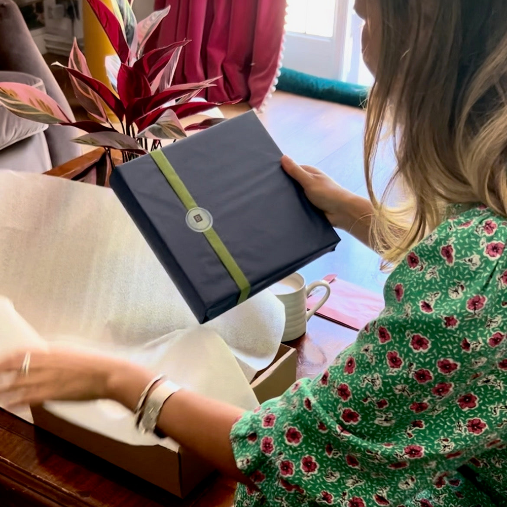 
                      
                        There is a woman in a green floral dress who is holding a begolden order in her hands. The begolden order has been wrapped in blue tissue paper.
                      
                    