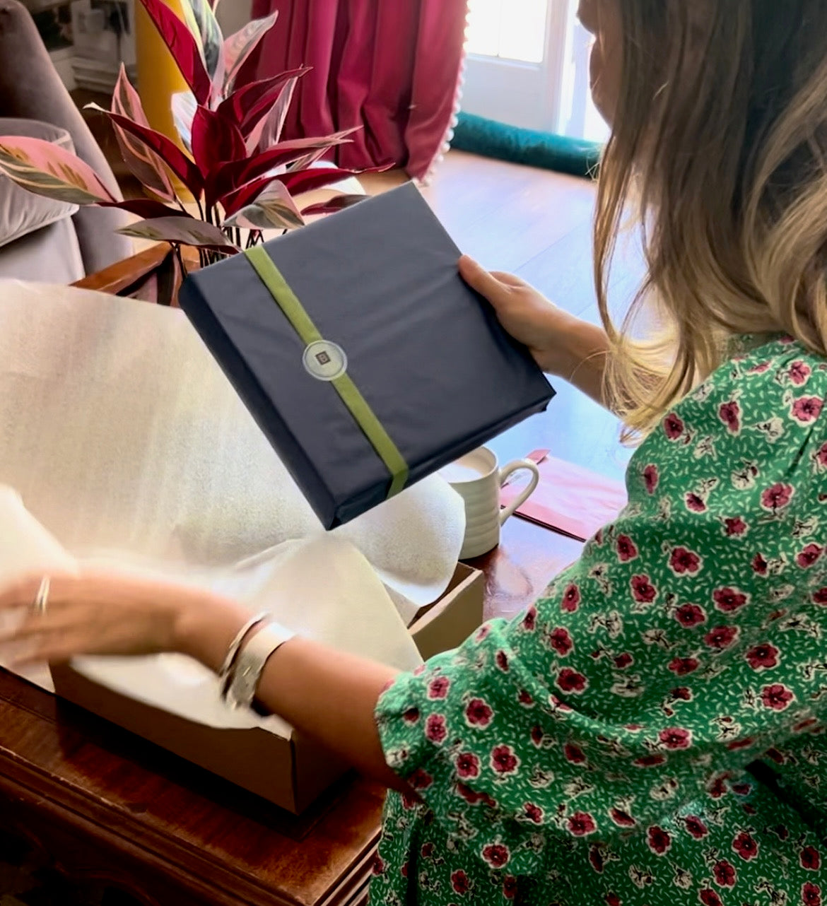 a woman is opening her begolden order. The photo album is wrapped in navy tissue paper