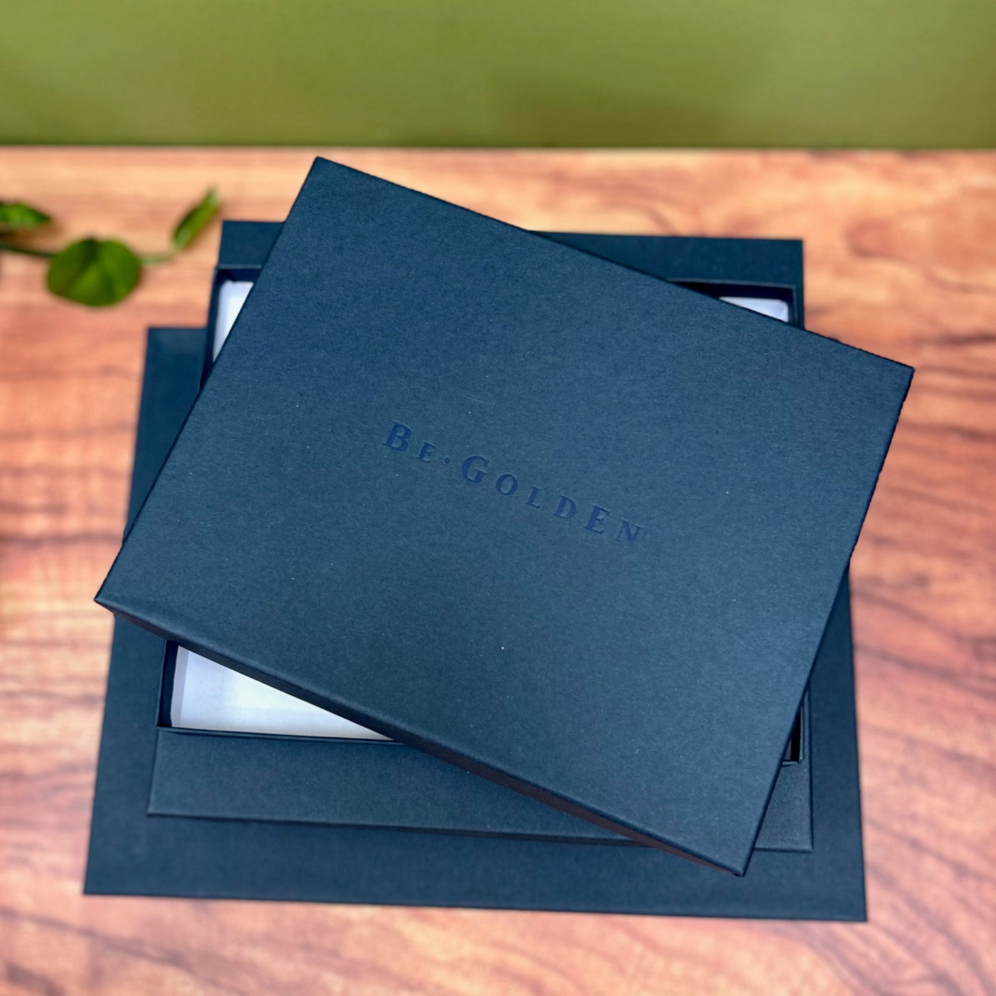 a pile of navy blue presentation boxes are sitting on a wooden table. You can see that they have been stamped with the name begolden on the front