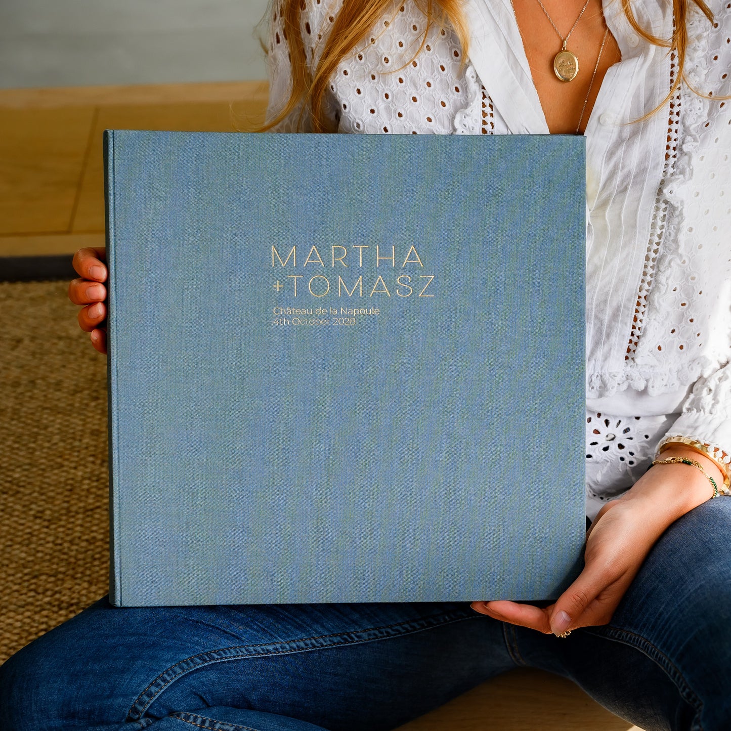 A woman holds a large, linen wedding photo album, printed with two names and wedding details