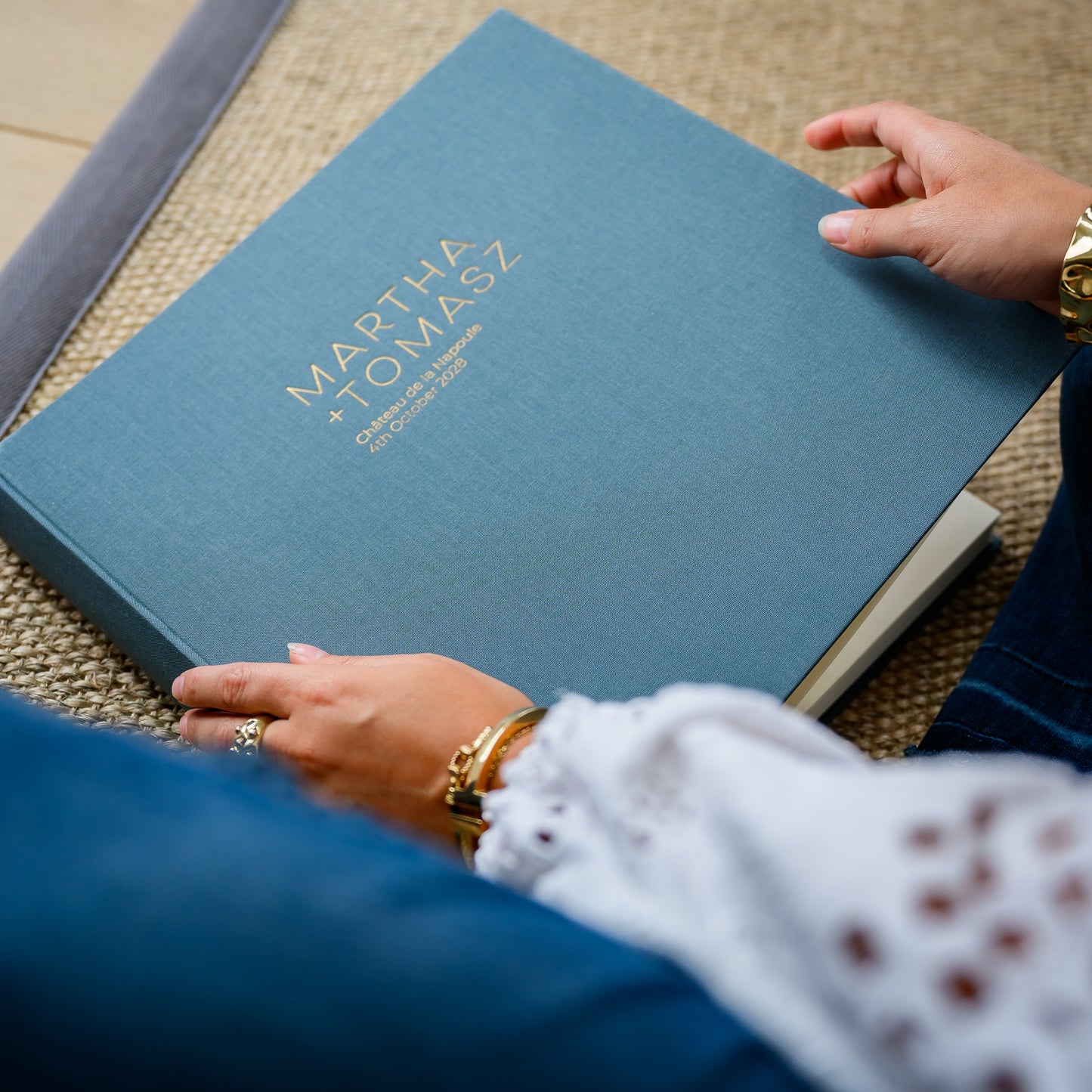 A woman holds a large, grey linen wedding photo album, printed with two names and wedding details