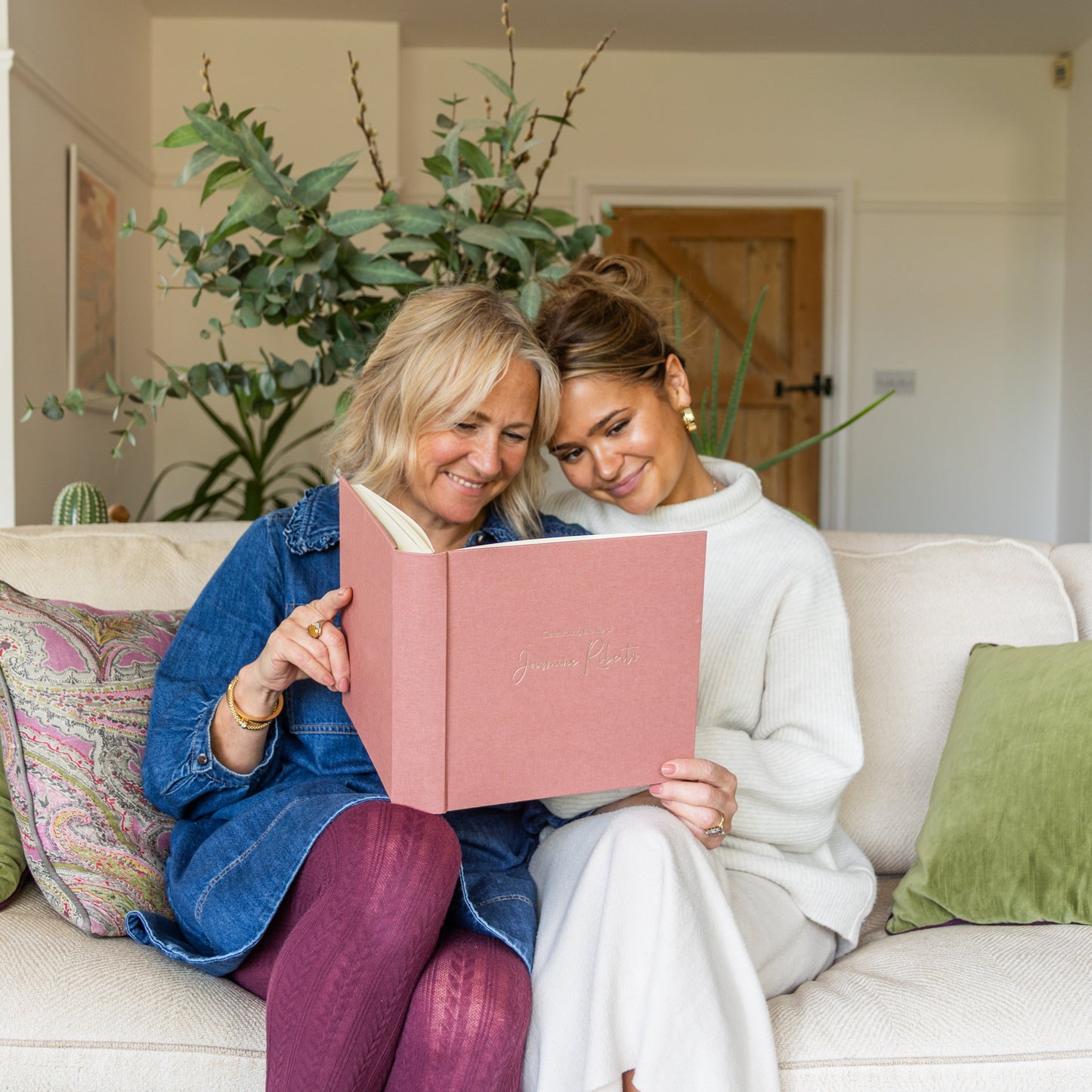 Two women sitting on a couch, looking at a personalised condolence book together.