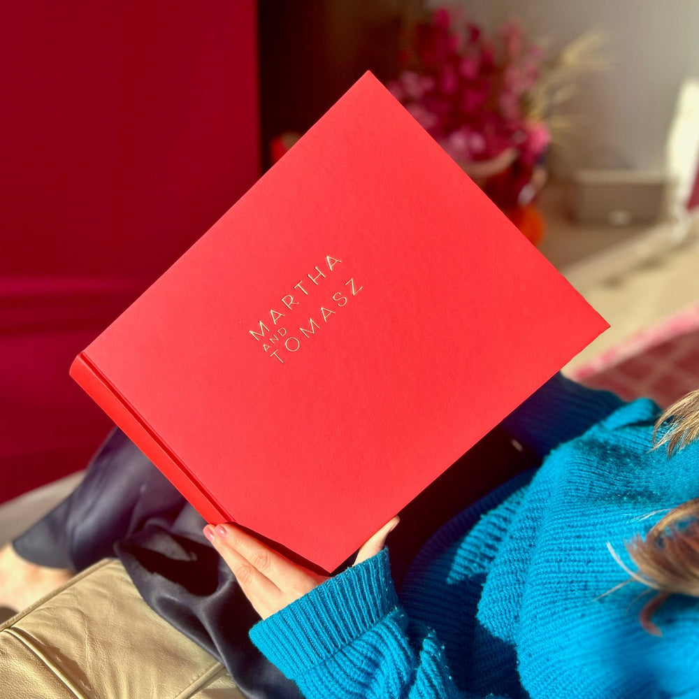 There is a woman sitting on a chair holding a red guest book allowing a front view of the book. 