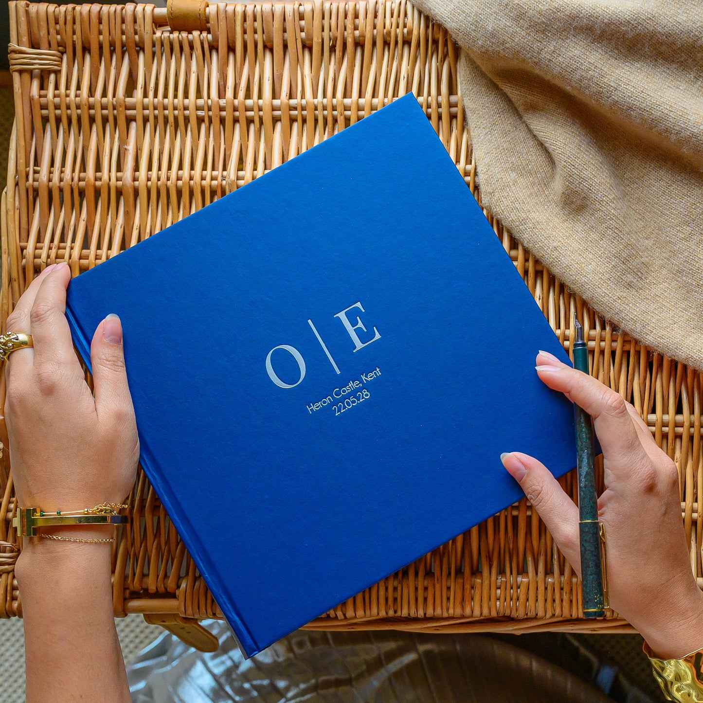 Woman holding a personalised wedding guest book with 'O&E' hand printed on the front, on a wicker surface. 
