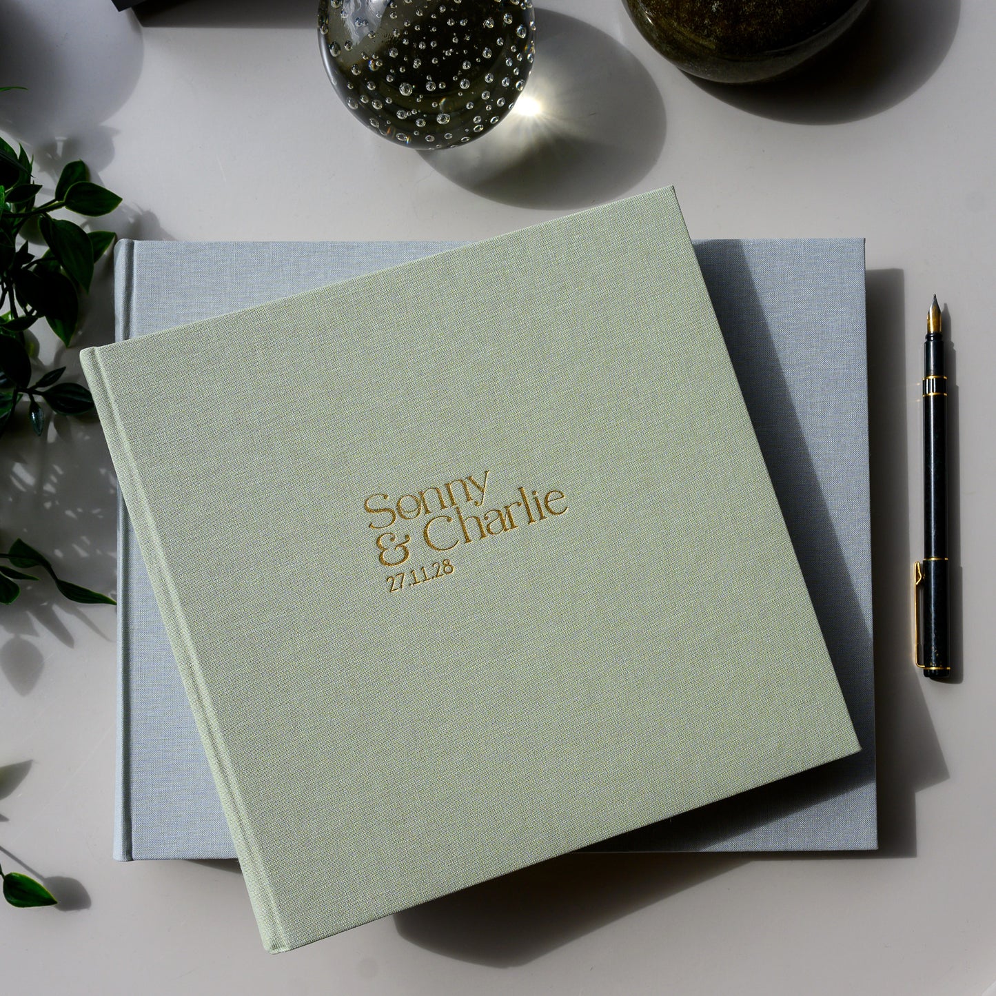 Woman holding a pale green wedding guest book personalised with the printed names 'Sophie & Charlie' on the cover.