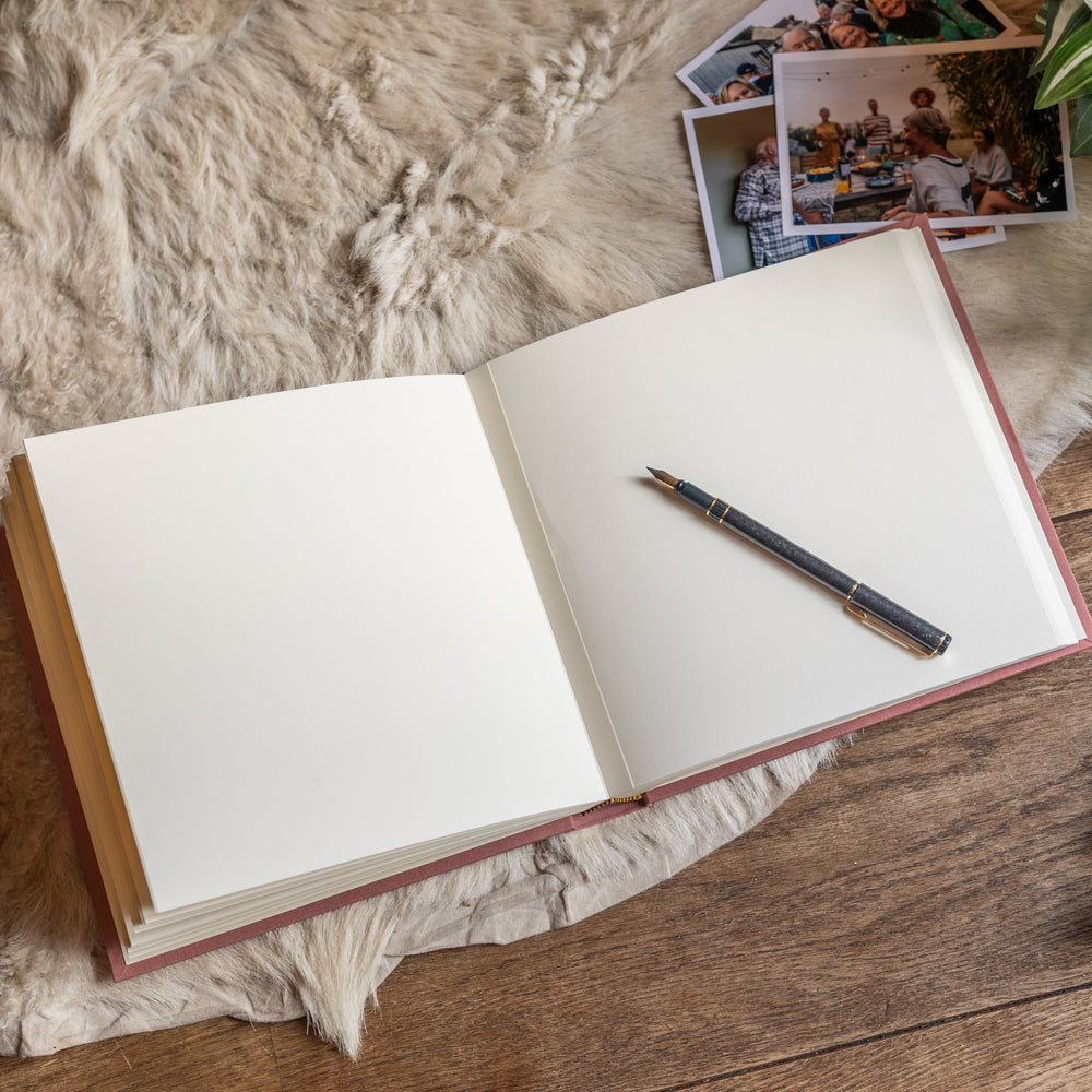 
                      
                        A condolence book lies open on a white goatskin rug. You can see the plain pages inside. There is a fountain pen resting on one of the pages and there are also photos tucked under one of the corners.
                      
                    