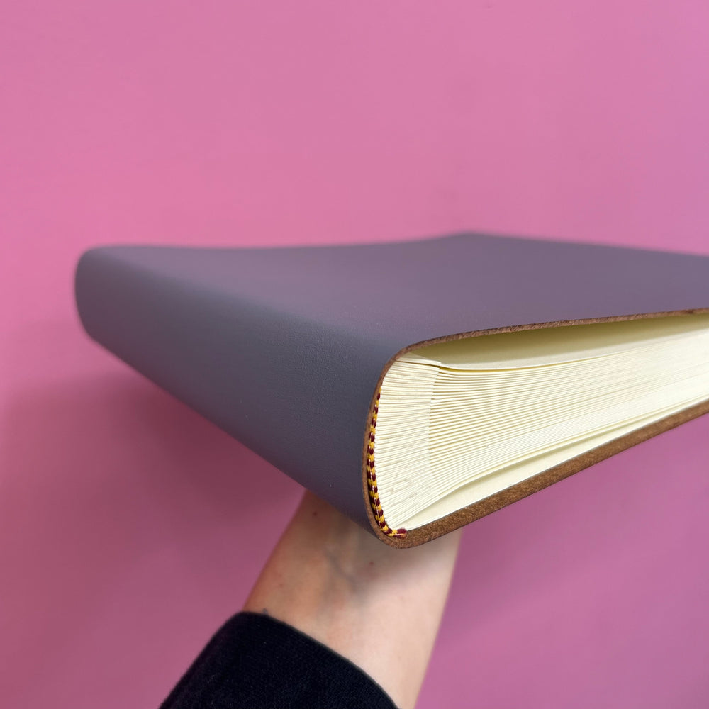 
                      
                        There is a woman holding up a condolence book allowing the customer to see the inside of the book, and the bind. 
                      
                    