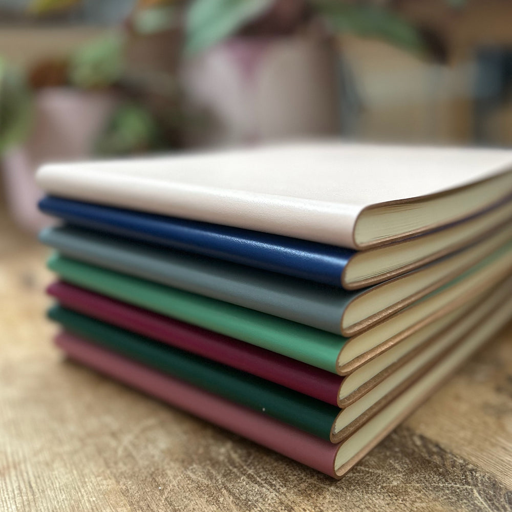 
                      
                        A pile of leavers books are on a wooden table and you can see all the different colours of the books. You can also see the interior of the books. 
                      
                    