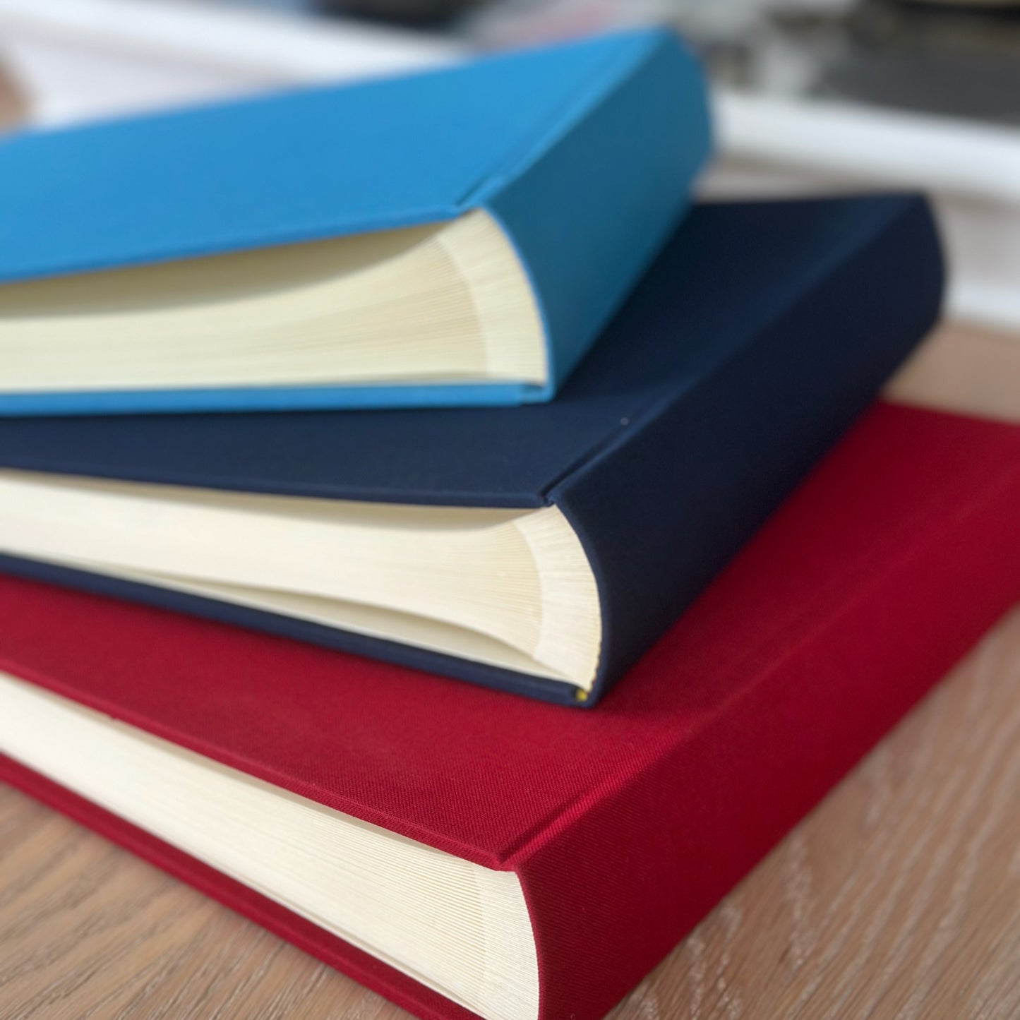 Stack of linen-bound books with blue, red, and navy covers on a wooden surface.