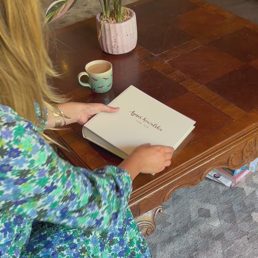 A lady with a cup of tea about to look through and album resting on the coffee table