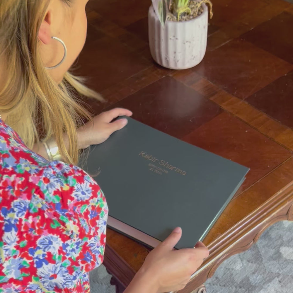 a woman looks through a large corporate leavers book. It is black with company details on the front. It is made by BeGolden