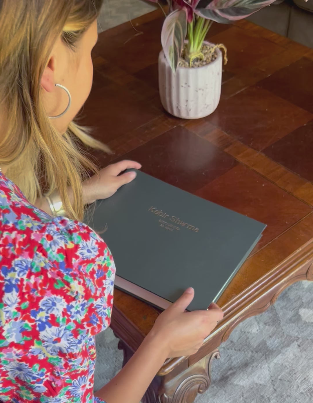 a woman looks through a large corporate leavers book. It is black with company details on the front. It is made by BeGolden