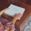 the video shows someone leafimg through the wedding guest book, stroking the front and turning it over. it has been printed on the front with gold lettering 
