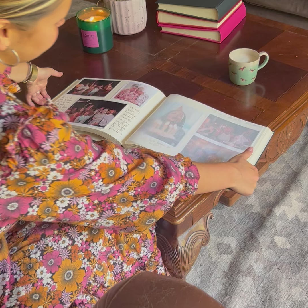 a video of a lady in a floral dress flicking through a phot album filled with memories