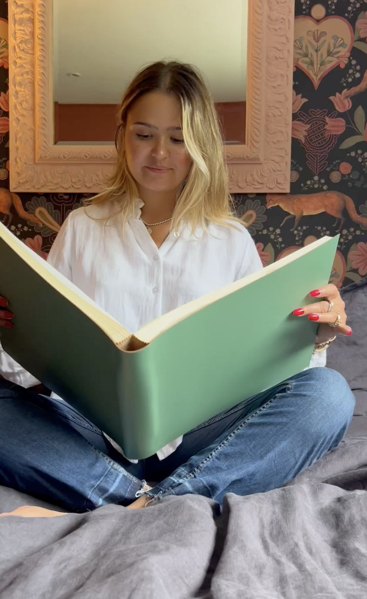 Short video of a girl sitting on a bet looking through a green photograph album