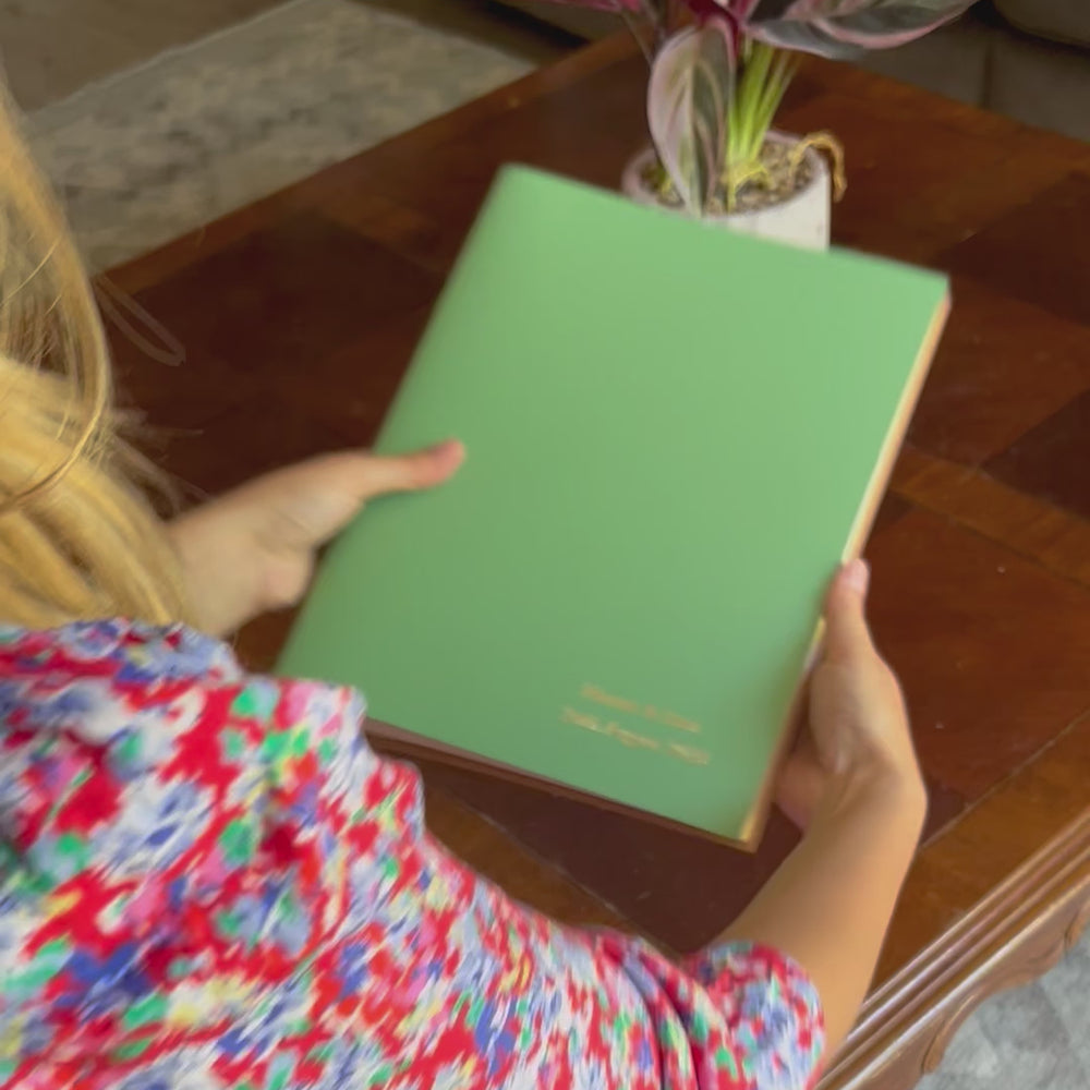 
                      
                        Load and play video in Gallery viewer, A video of a young woman flicking through a green A4 photo album that has been personalised on the front. She places it on a coffee table where there is a house plant. 
                      
                    