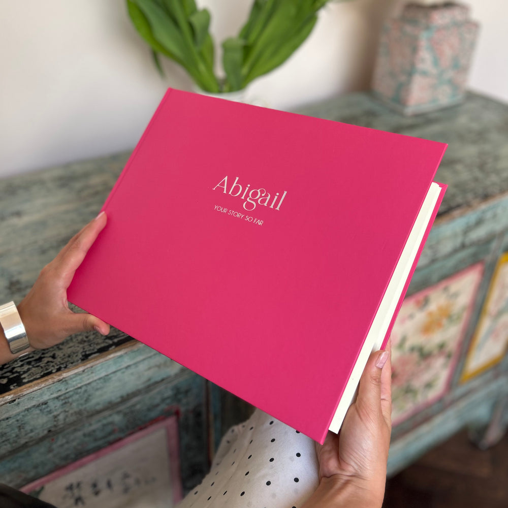 
                      
                        There is a woman holding a landscape album in the shade strawberry. This vibrant pink album has a name printed on the front in silver hot foiling. 
                      
                    