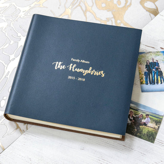 on a table lies a navy blue leather album which has been personalised with gold writing