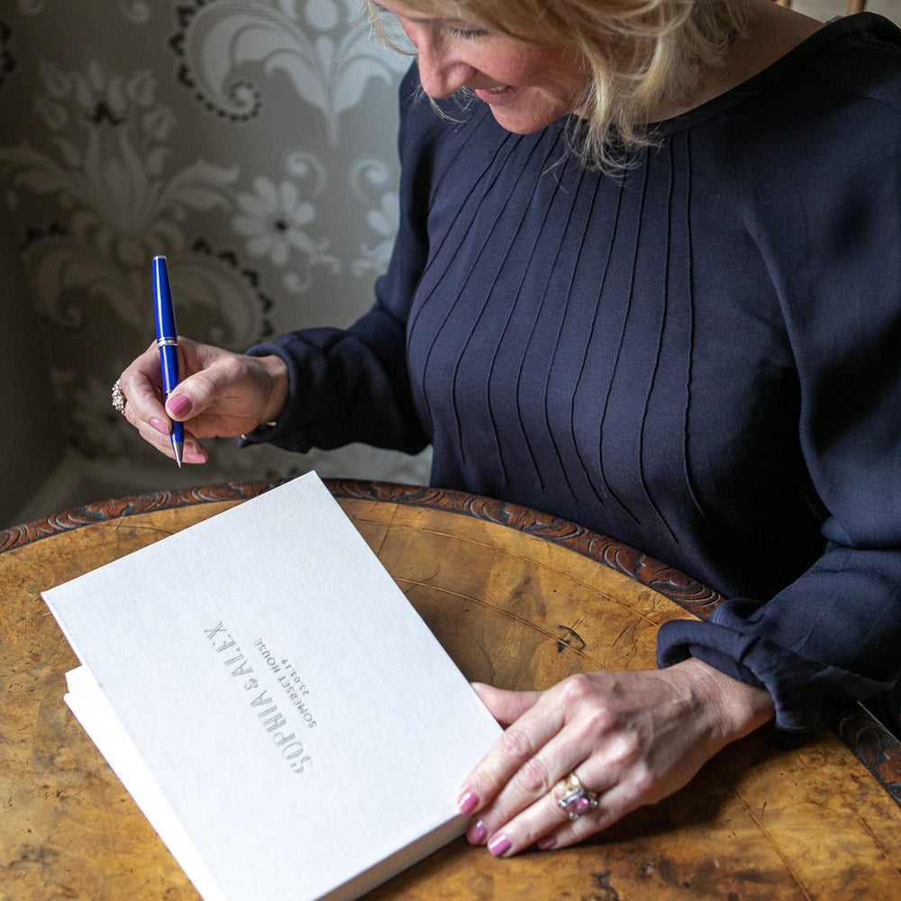 
                      
                        an ivory linen wedding guest book is ready to be signed by a wedding guest
                      
                    