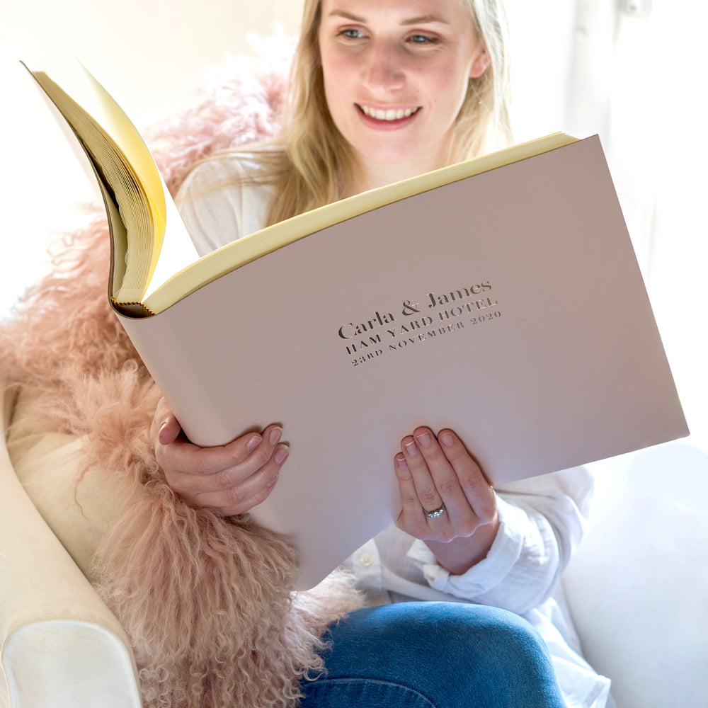 
                      
                        A woman sits in an armchair looking through her wedding photo album. It has been printed on the front with her wedding details.
                      
                    
