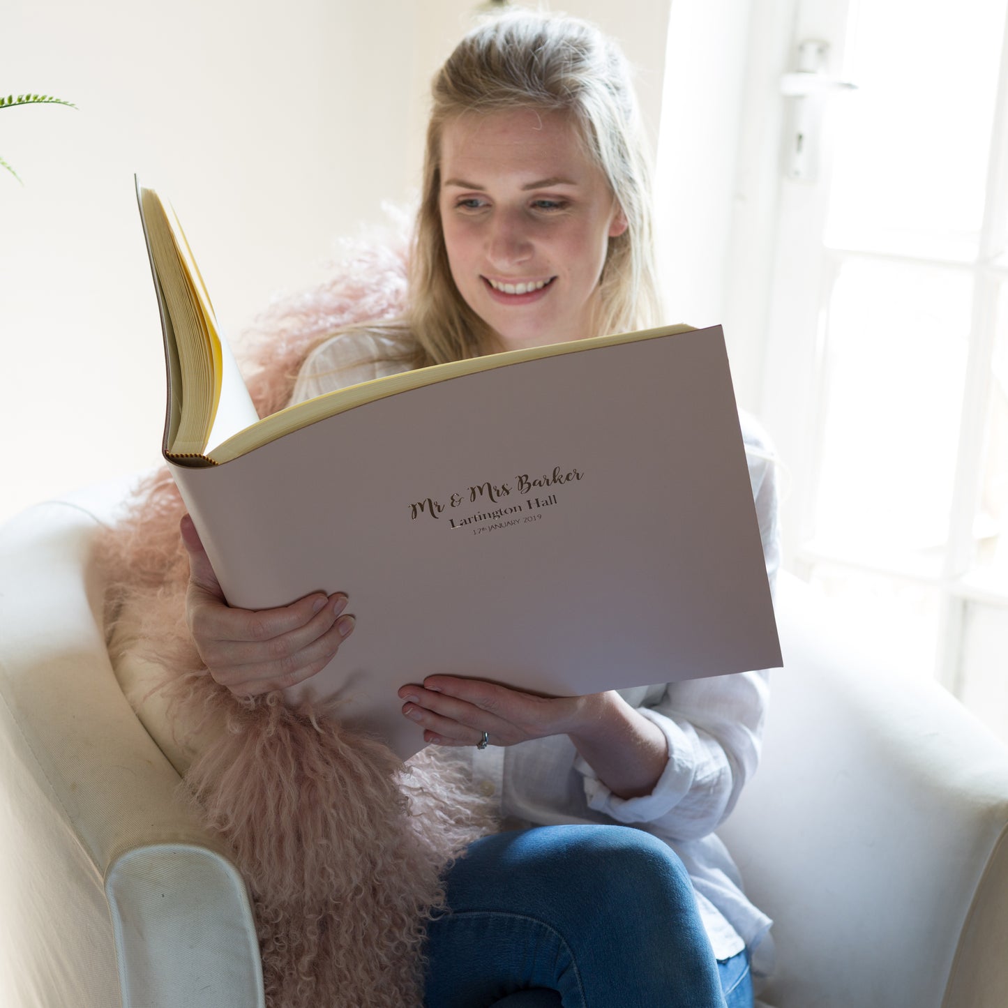 There is a woman looking through her large leather album which has been personalised on the front. 