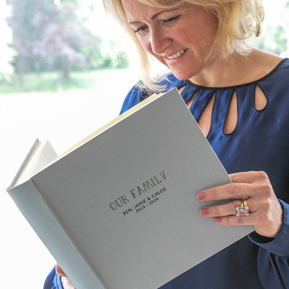 
                      
                        a lady smiling as she looks through a family photograph album
                      
                    