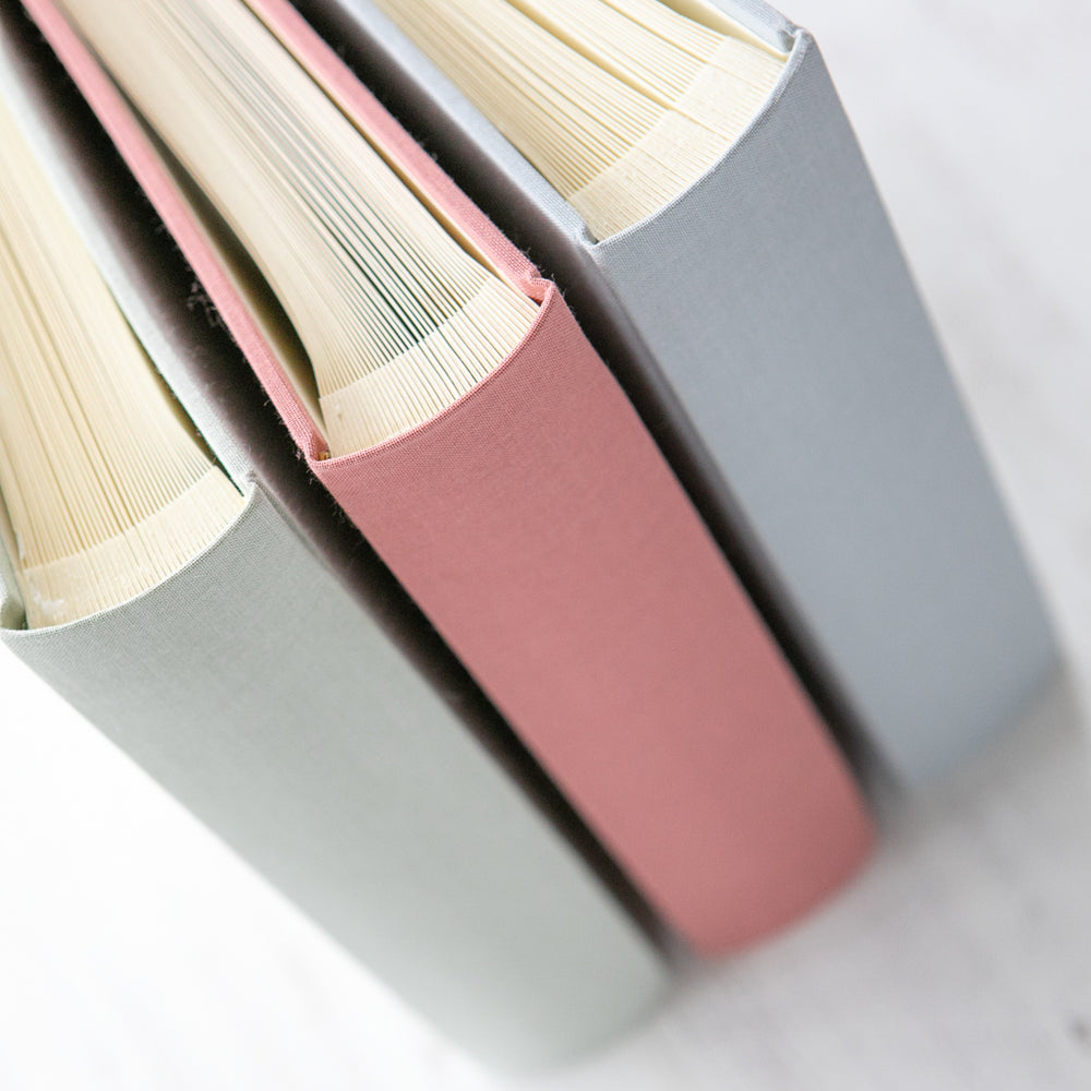 
                      
                        There are three linen albums stood up next to one another. You can see the bind and the interior of the three books.
                      
                    