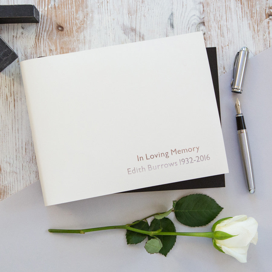 a personalised condolence book lies on a table with a white rose and a pen